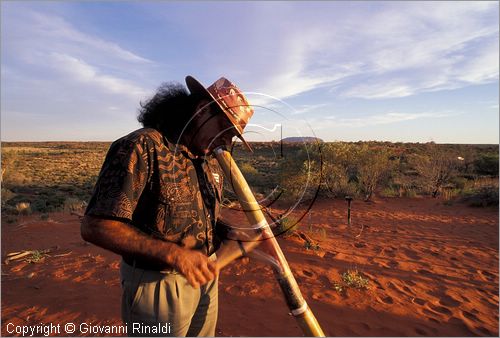 AUSTRALIA CENTRALE - Uluru Kata Tjuta National Park - un aborigeno suona i "didgeridoo", strumento musicale tradizionale - sullo sfondo il Ayres Rock