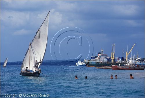 TANZANIA - ZANZIBAR  (Oceano Indiano) - Stone Town - la tipica barca a vela latina dei pescatori passa vicino ia bambini che fanno il bagno